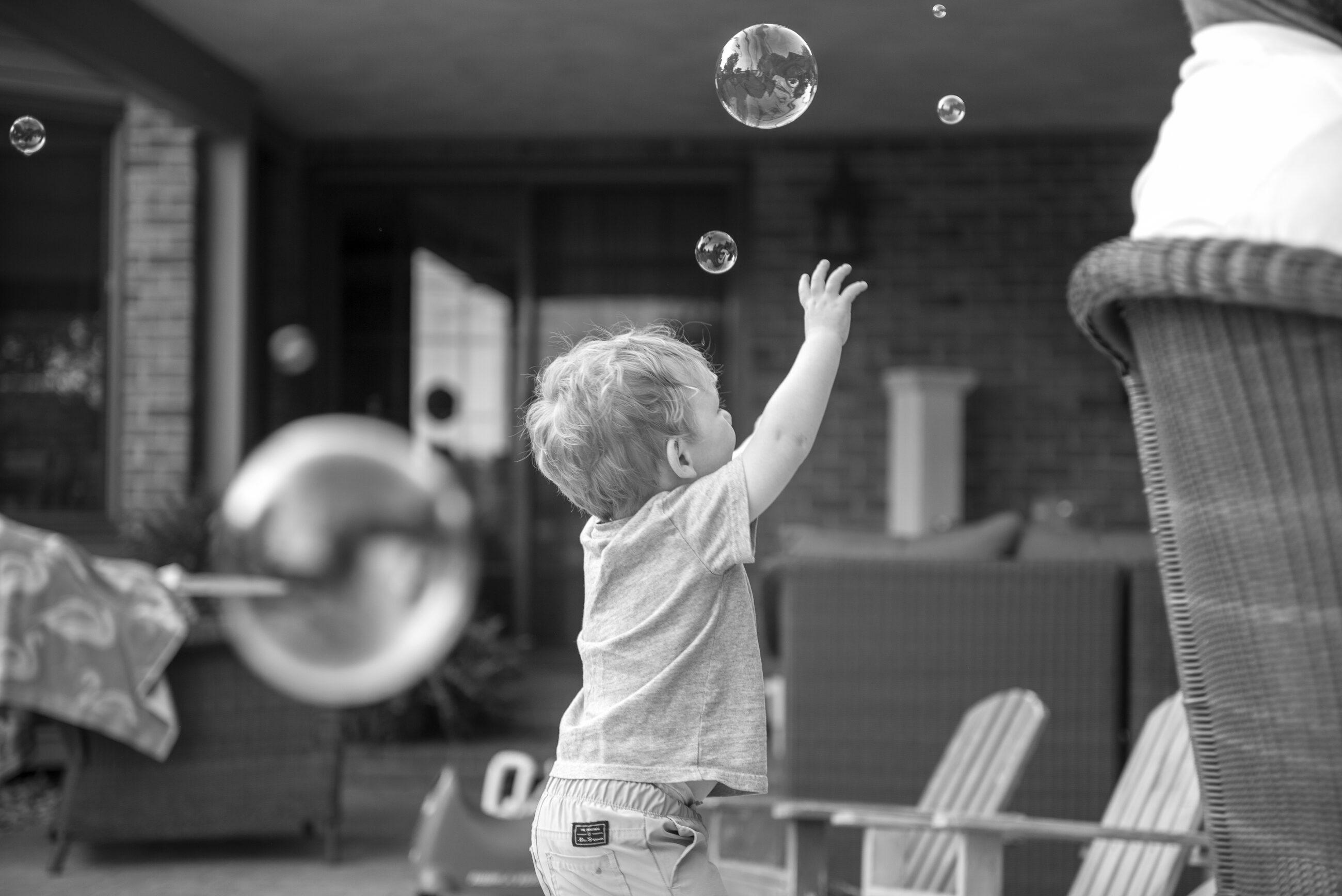 A child reaching for soap bubbles in black and white