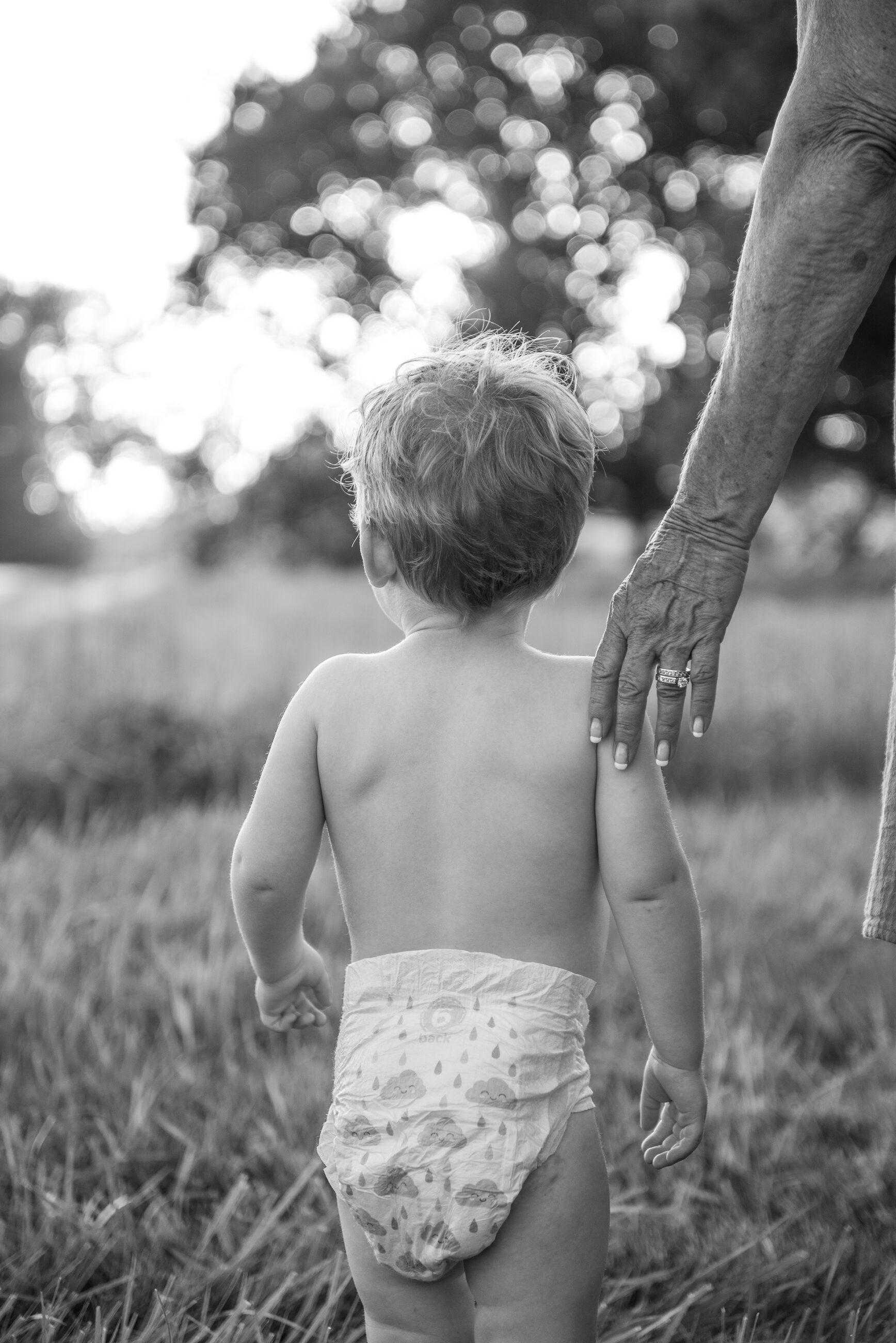 A grandparent's hand reaching for a toddler in the tall grass, black and white
