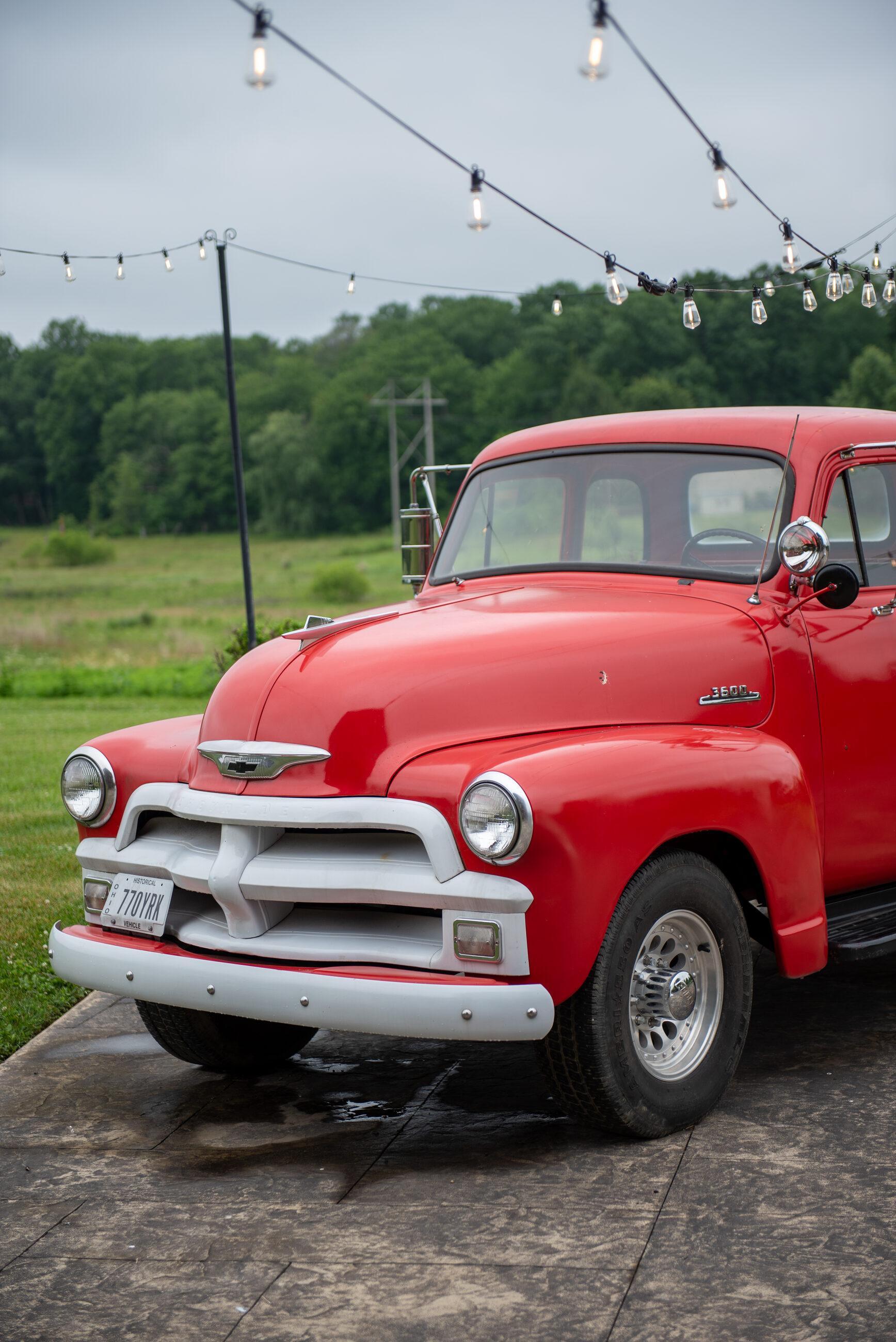 A red 1954 pickup parked beneath string lights before the storm